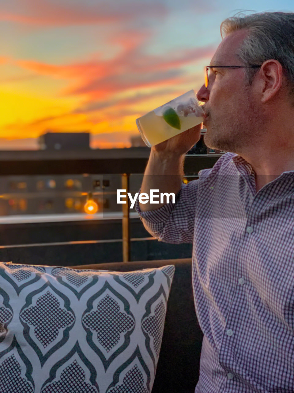 Mature man having drink against sky during sunset