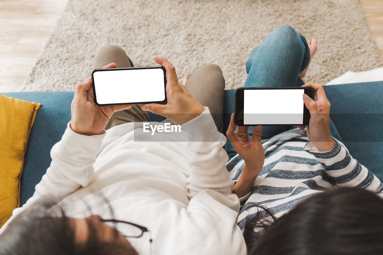 Directly above shot of couple using phone while sitting on sofa at home