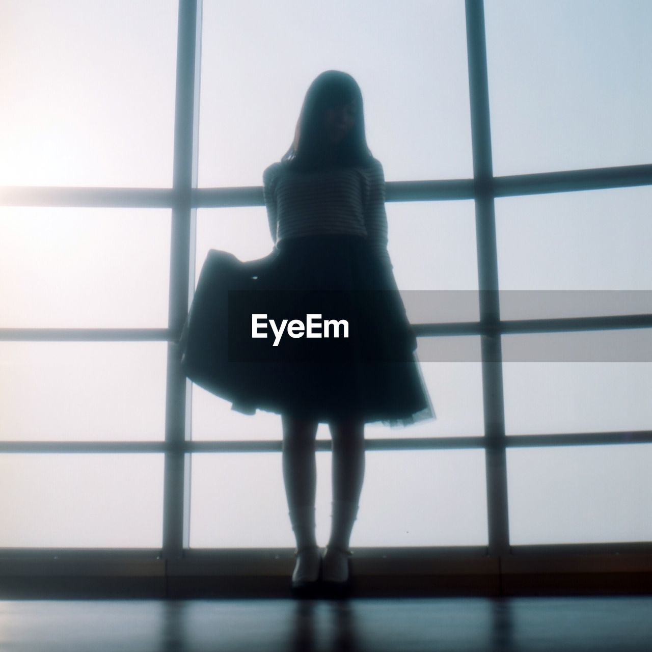Surface level view of silhouette woman holding skirt while standing against window