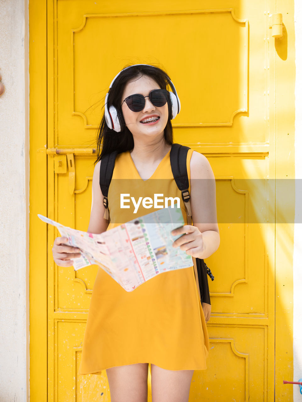 Smiling young woman holding map while standing against yellow door