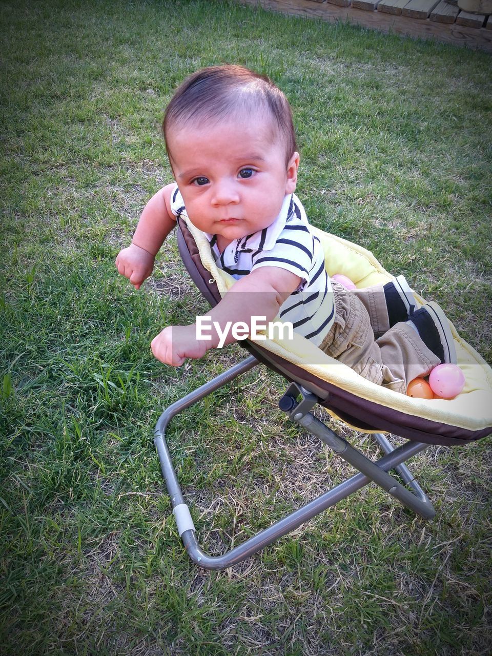 High angle portrait of cute baby boy on saucer chair at field