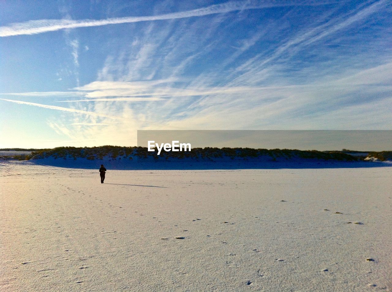 Scenic view of person walking at beach against interesting sky