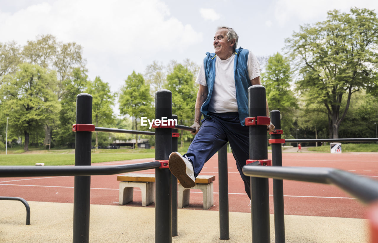 Smiling active senior man exercising on gymnastics bar at park