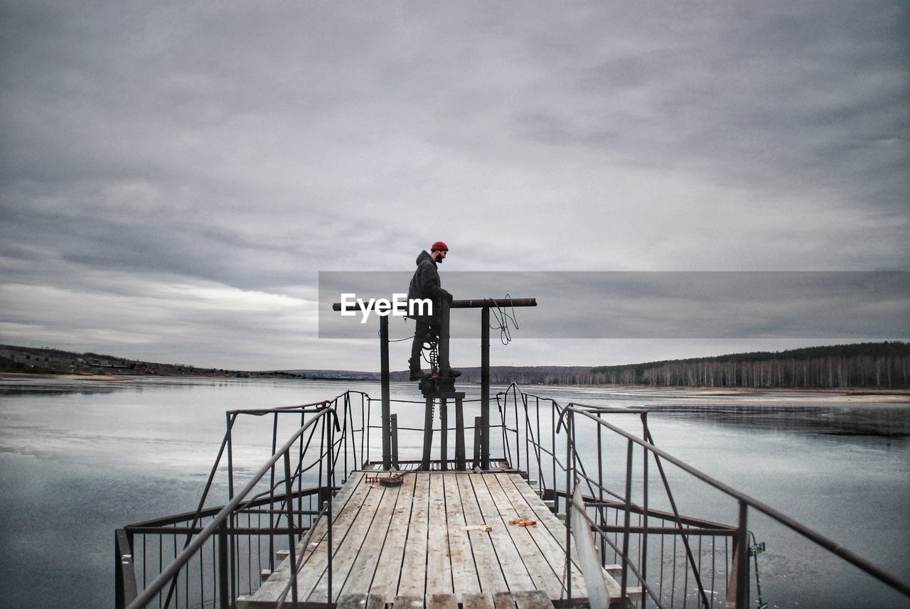 Man standing on pier over lake against sky