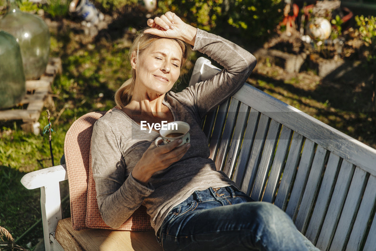 Woman with cup of coffee relaxing on garden bench