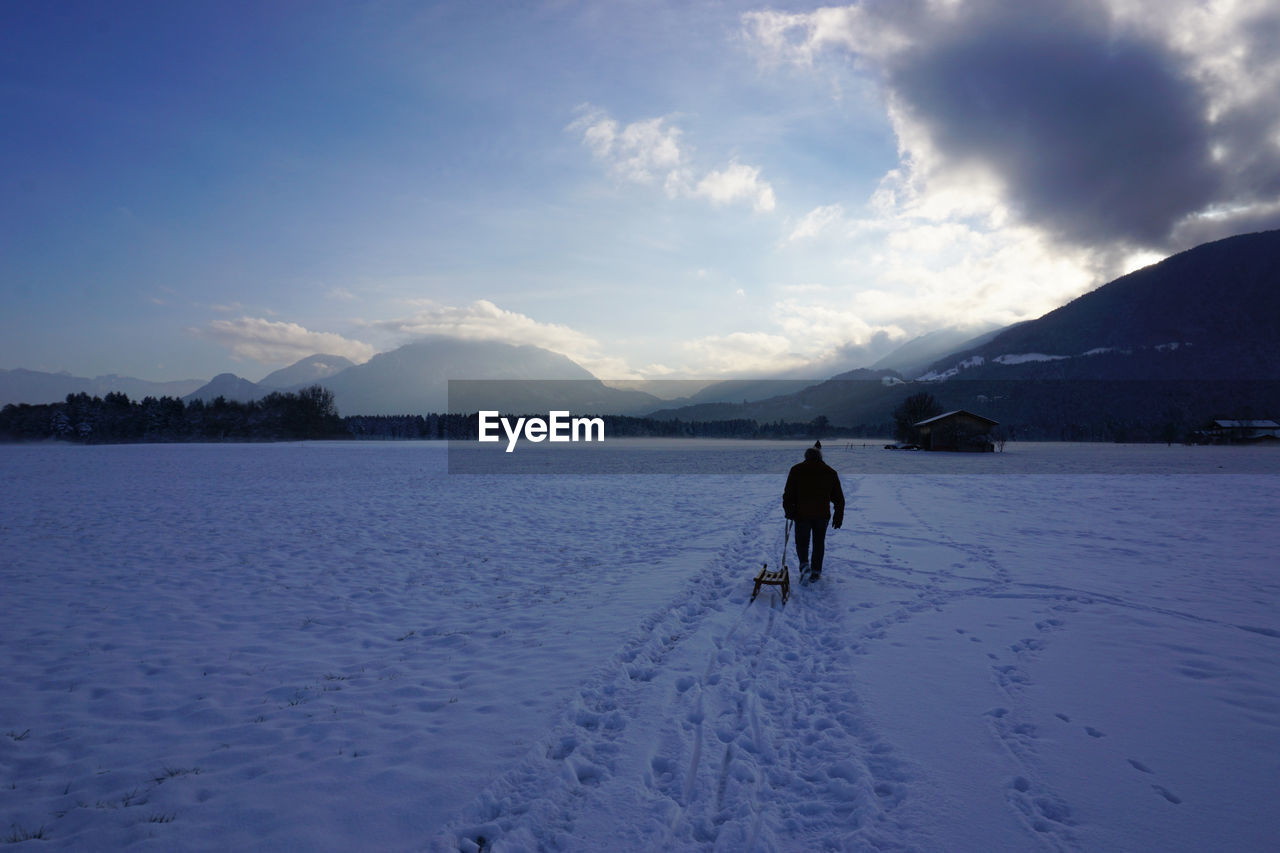 Man carrying sled on snow covered field