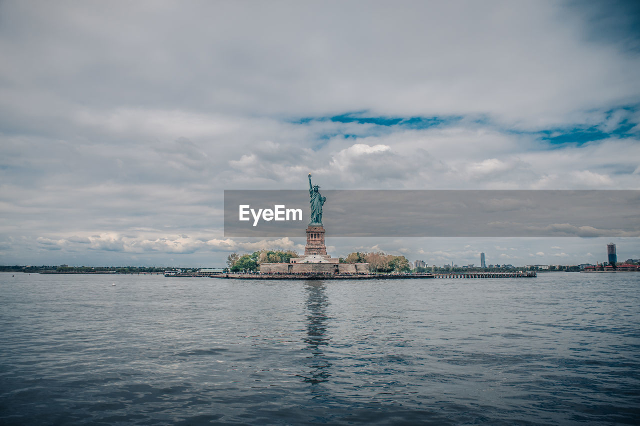 Statue of liberty by sea against cloudy sky