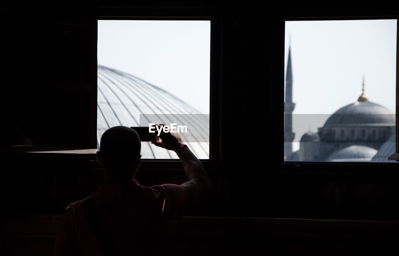 Rear view of man photographing through window