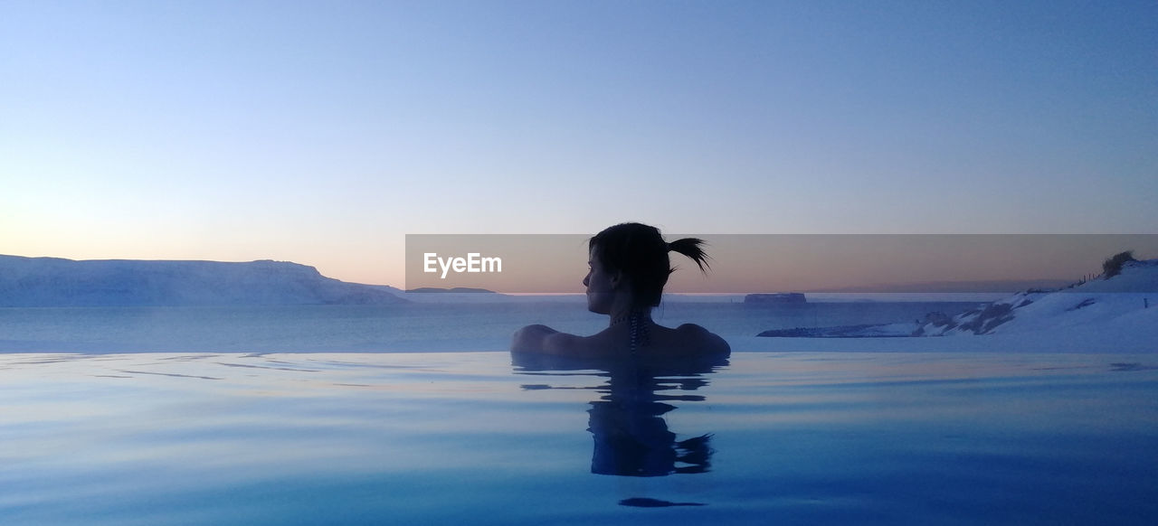 Silhouette woman in infinity pool against clear sky during sunset