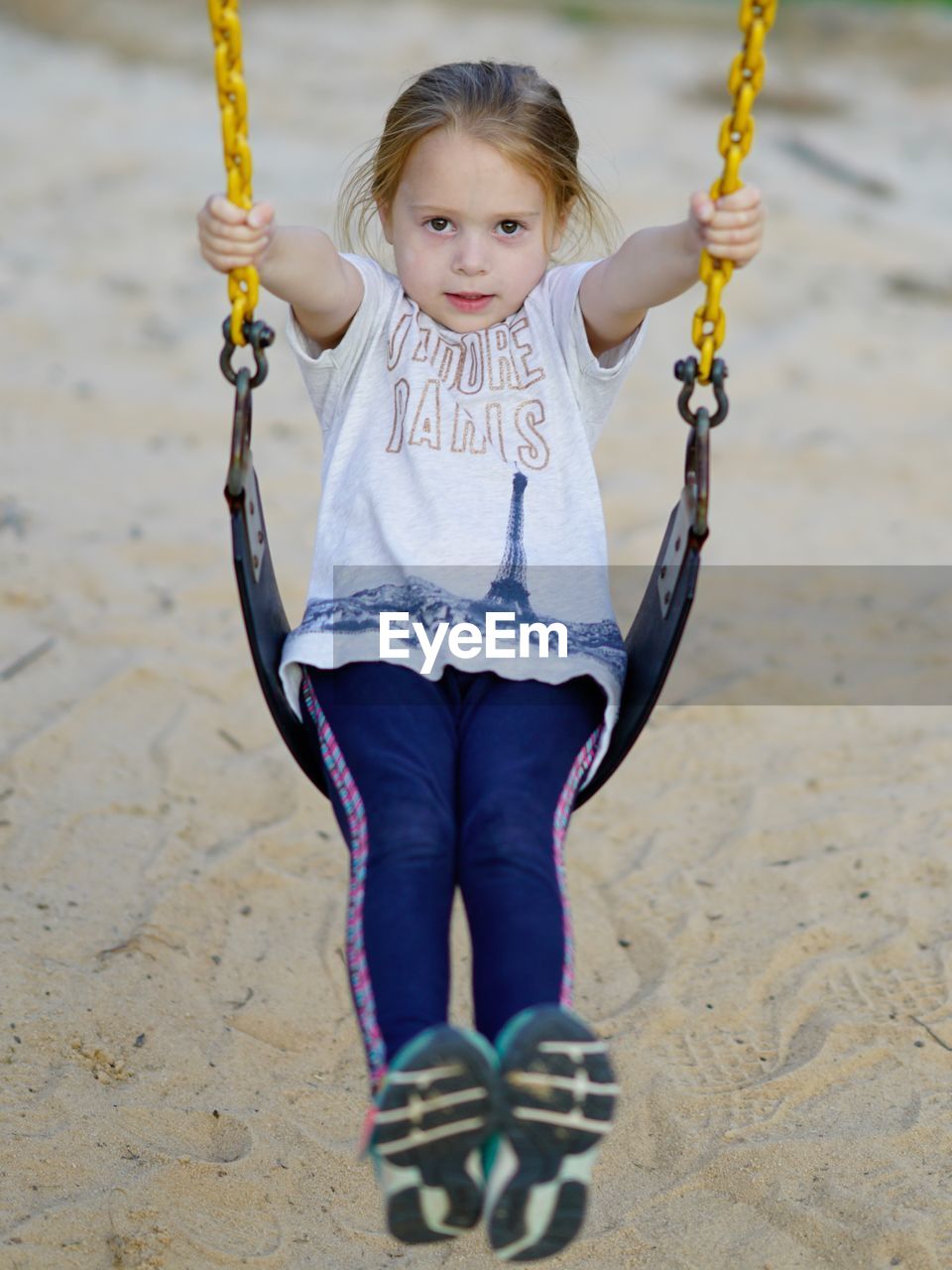 Girl swinging over sand in park