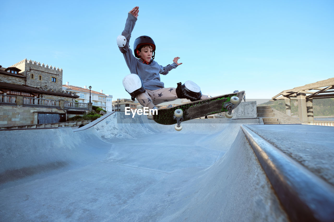 Teen boy in protective helmet riding skateboard in skate park on sunny day on seashore