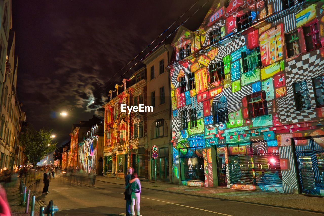 ILLUMINATED STREET AMIDST BUILDINGS AT NIGHT