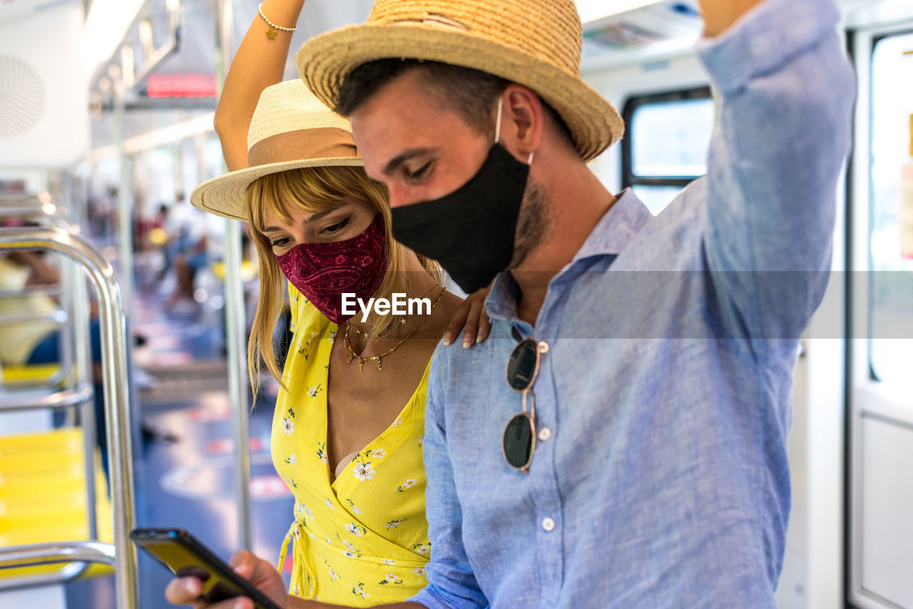 Smiling couple wearing mask using smart phone standing in bus