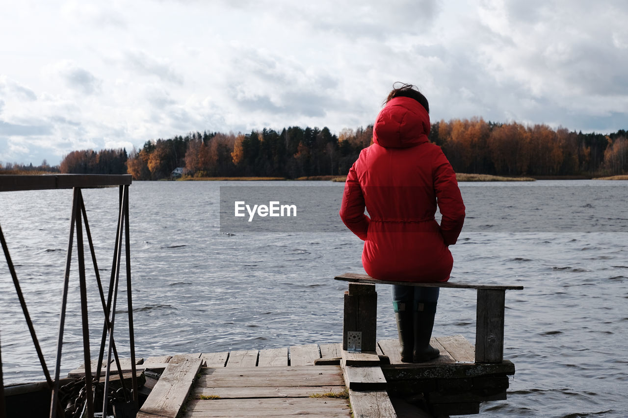 Woman in red jacket looks at the lake and sunset