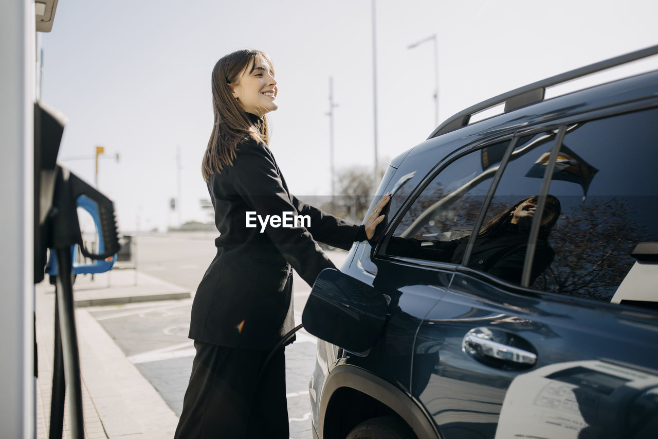 Smiling businesswoman charging electric car at charging station