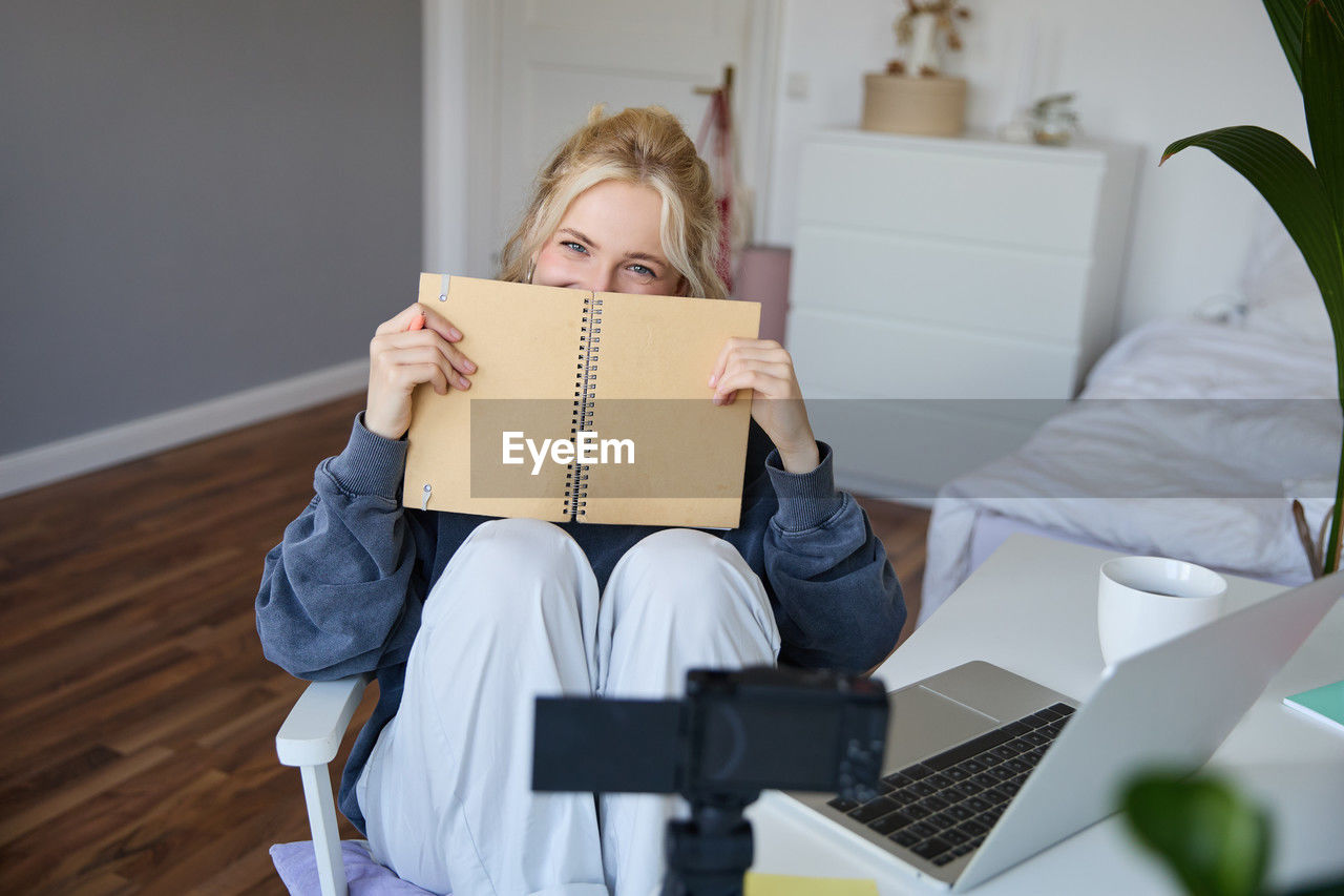 young woman using laptop while sitting on bed