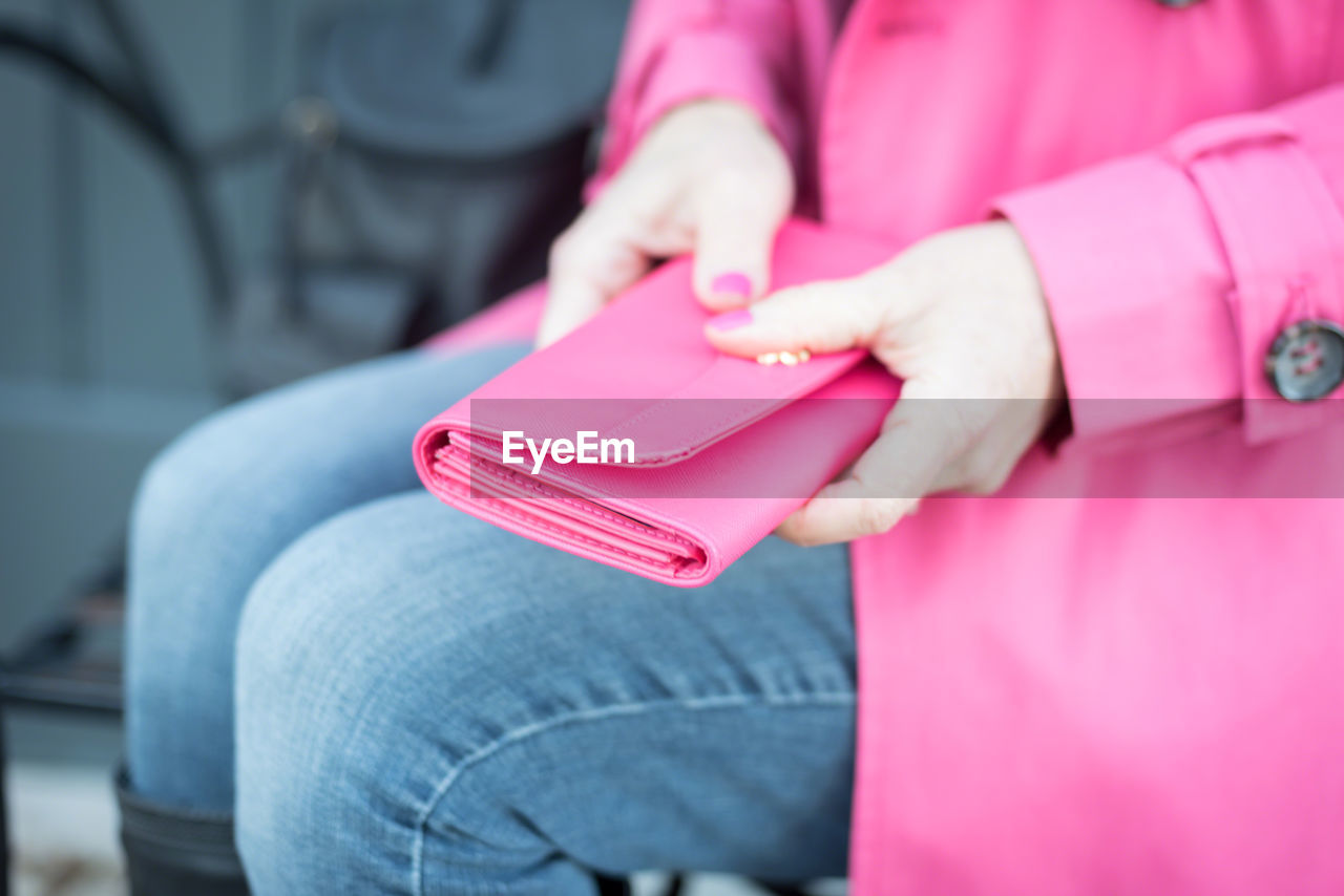 Midsection of woman holding pink purse while sitting outdoors