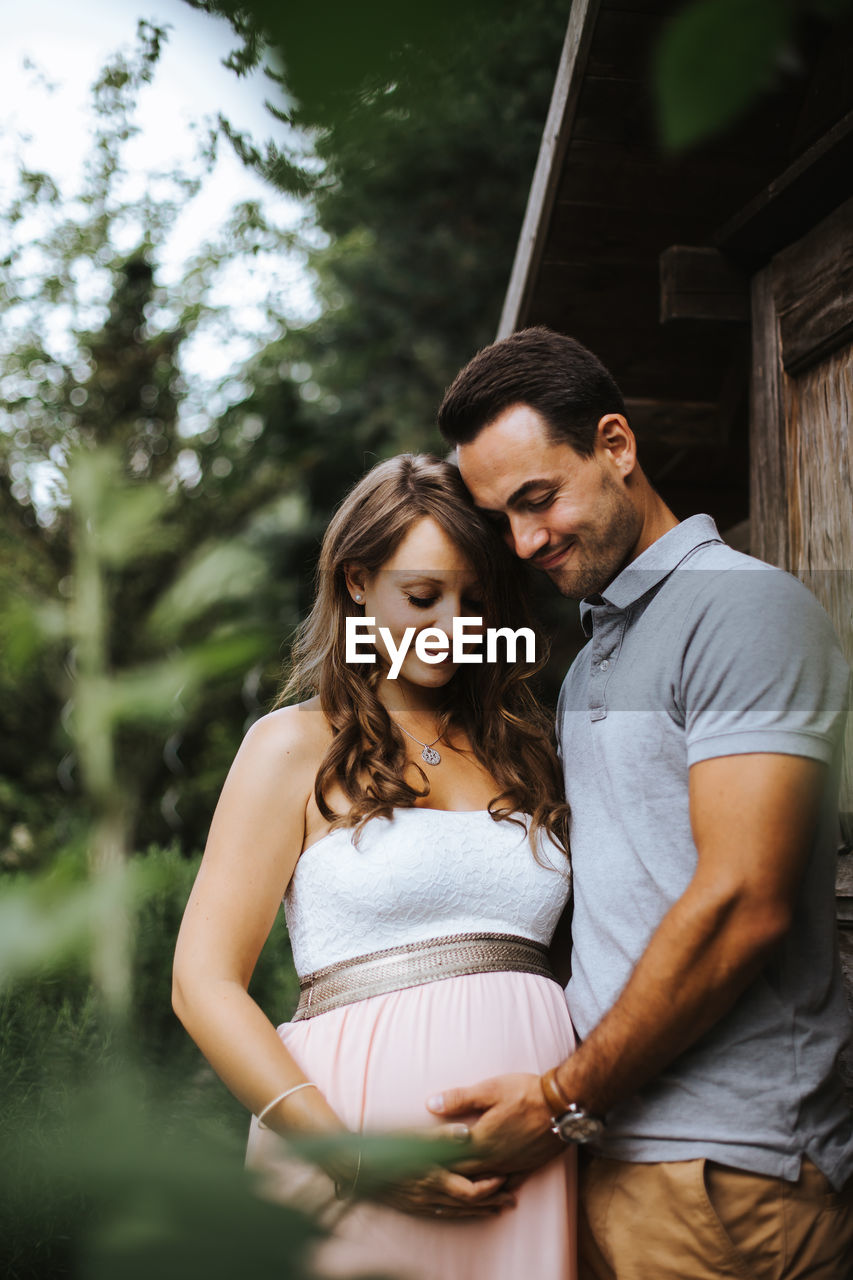 Low angle view of romantic couple standing against trees at park