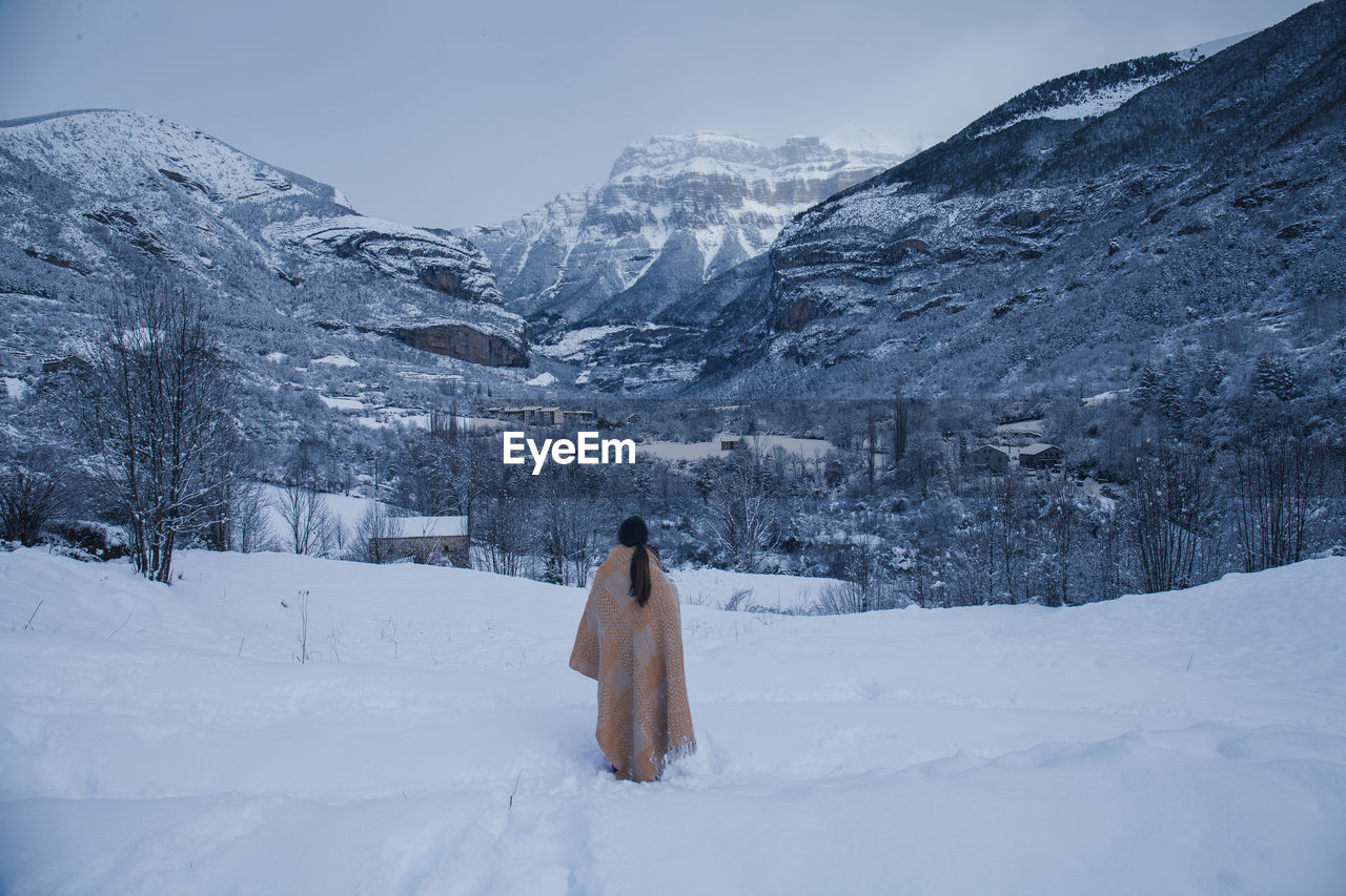 Rear view of woman wearing shawl while looking at snow covered mountain against sky