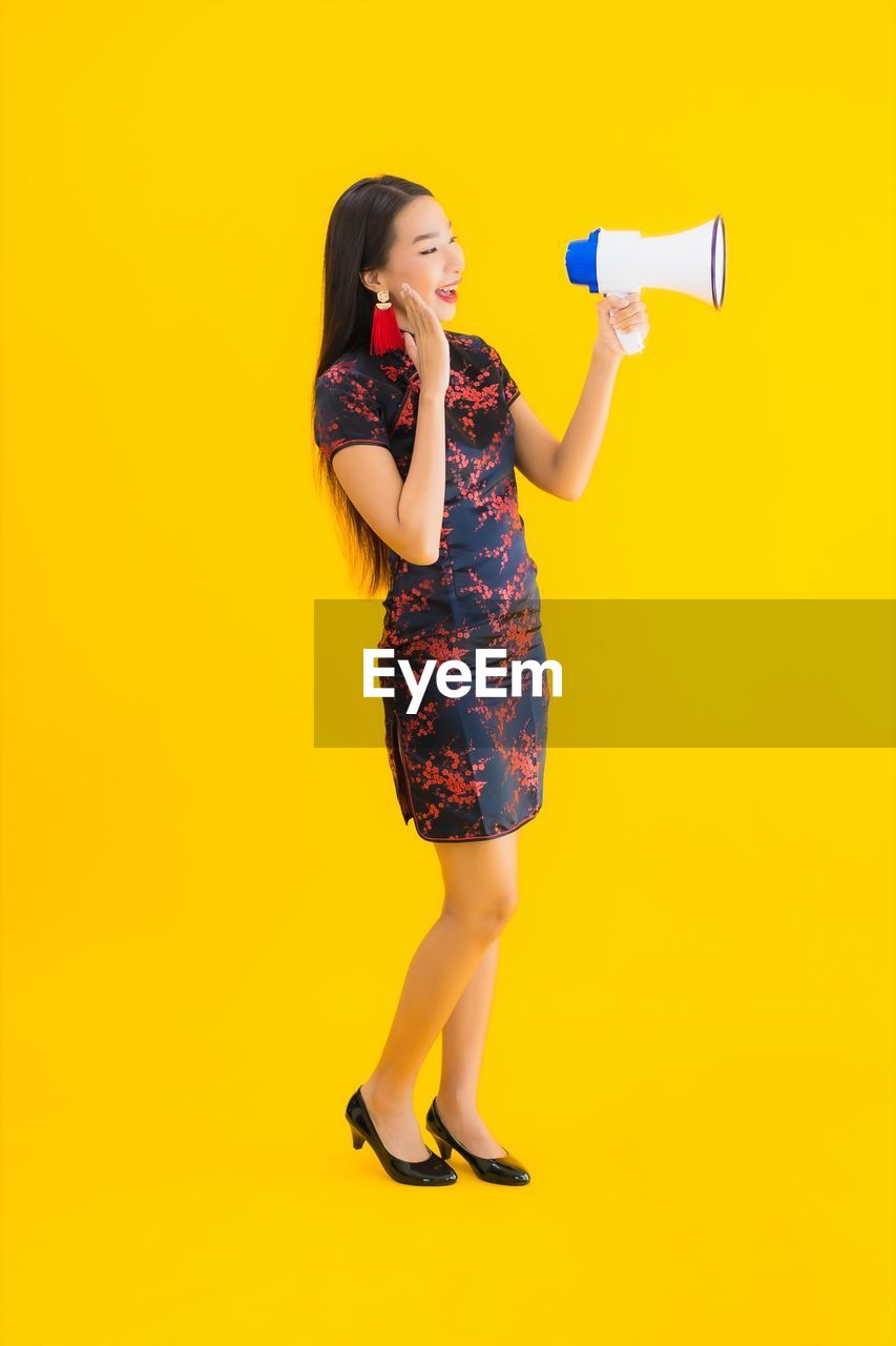 FULL LENGTH OF WOMAN STANDING AGAINST YELLOW WALL