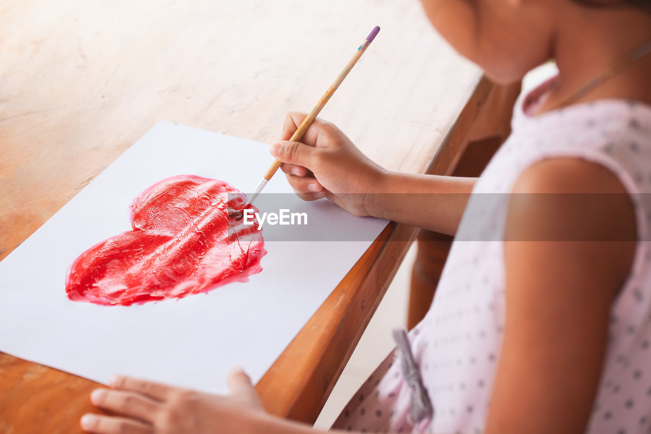 Midsection of girl painting heart shape on paper in porch