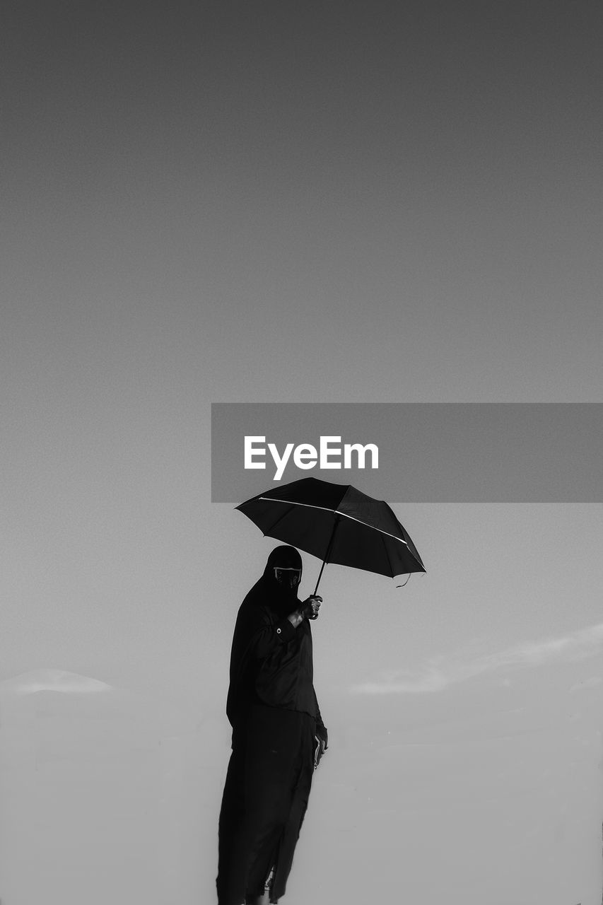 Woman holding umbrella standing against sky during rainy season