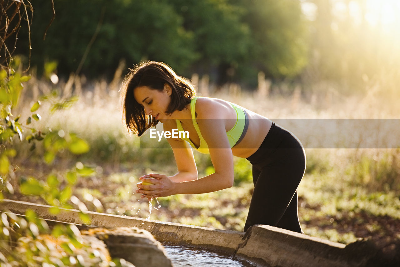 Young woman cleaning apple with water in forest