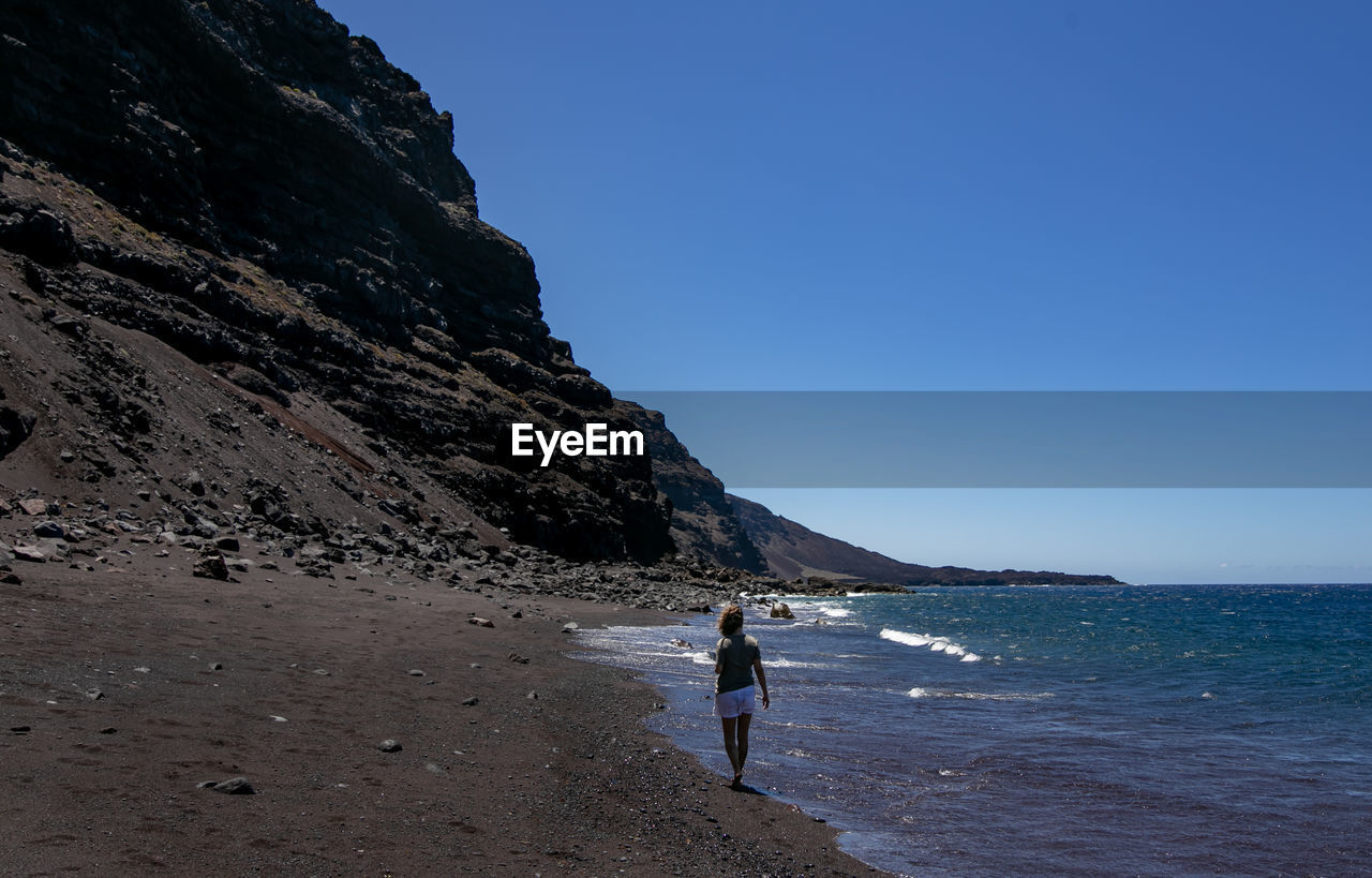 Woman on beach against clear blue sky