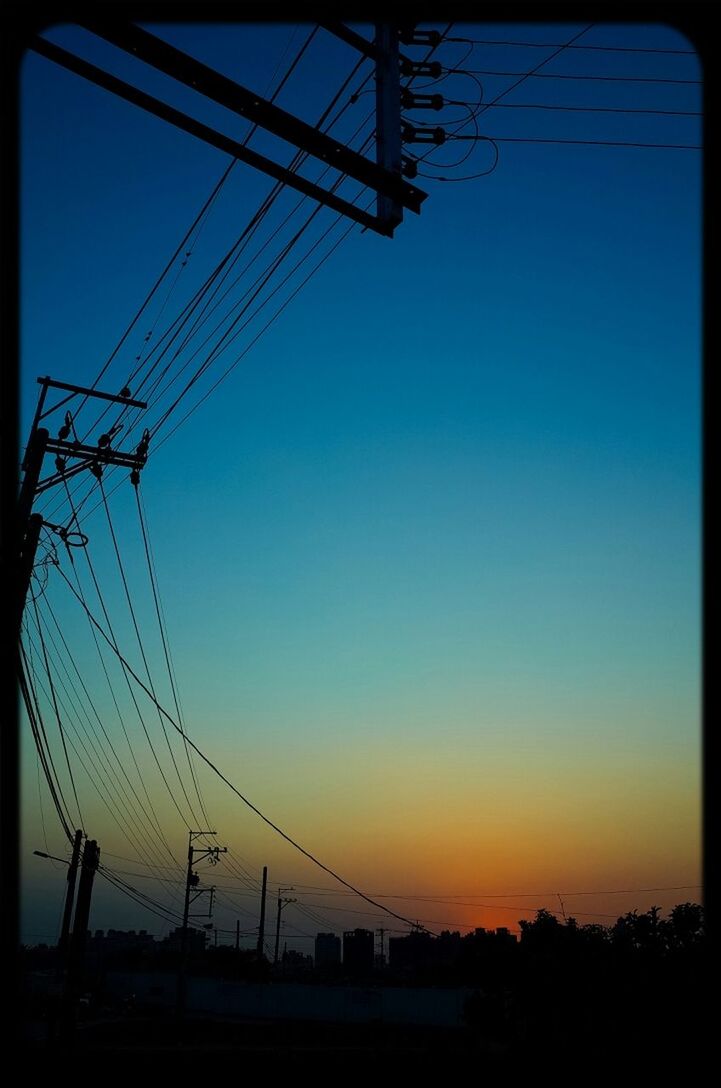 Low angle view of electricity pylons against blue sky
