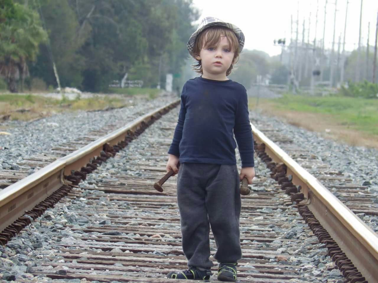 Portrait of boy holding nail on railroad track