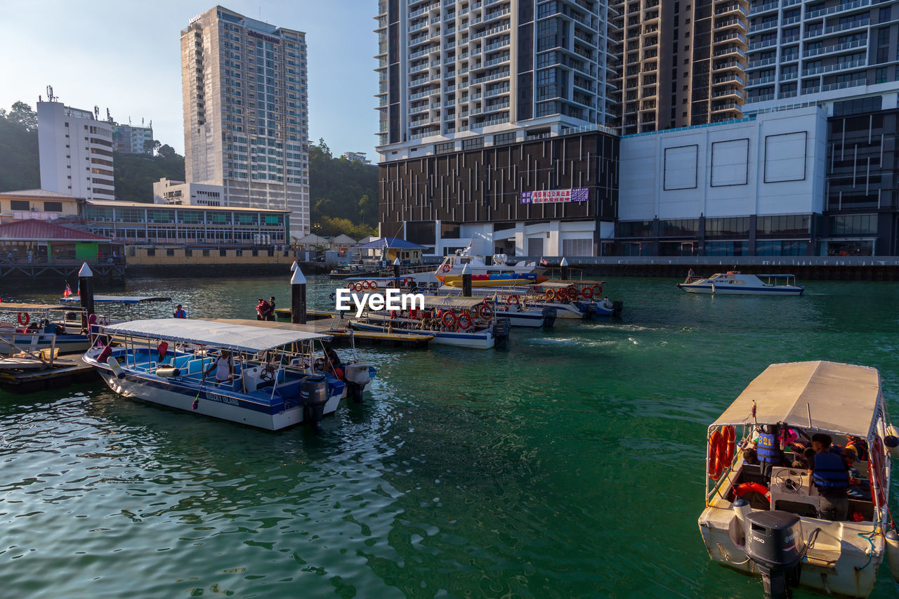 BOATS MOORED ON RIVER AGAINST BUILDINGS IN CITY