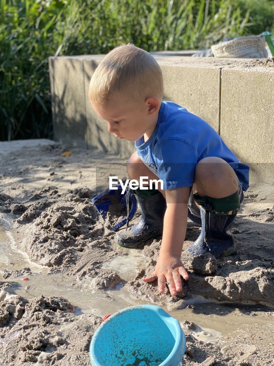 childhood, child, one person, men, full length, nature, casual clothing, day, sand, bucket, soil, innocence, land, toddler, leisure activity, lifestyles, looking, blond hair, looking down, container, outdoors, person, holding, digging, cute, sand pail and shovel, crouching, water, sunlight, summer, beach, standing