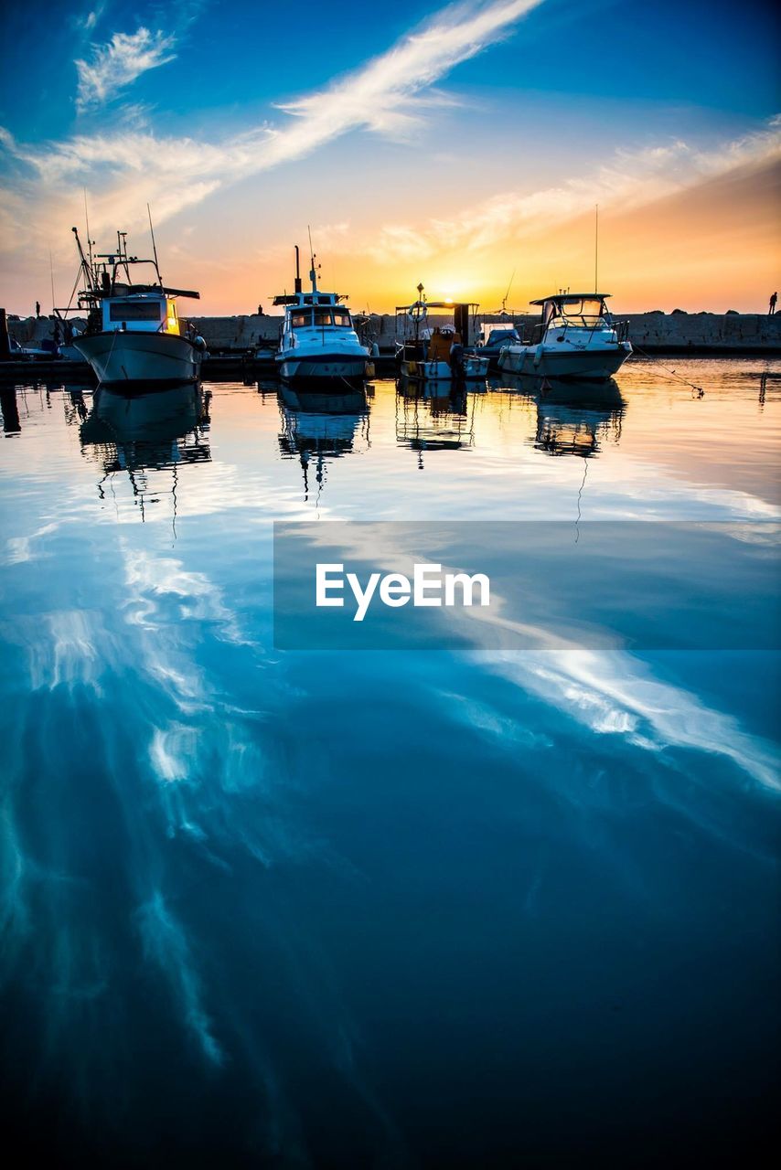 Boats moored in sea against sky during sunset