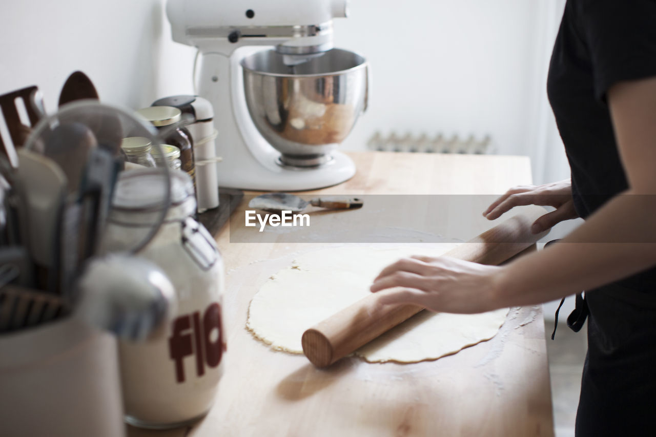 Midsection of woman rolling dough while working in kitchen at home