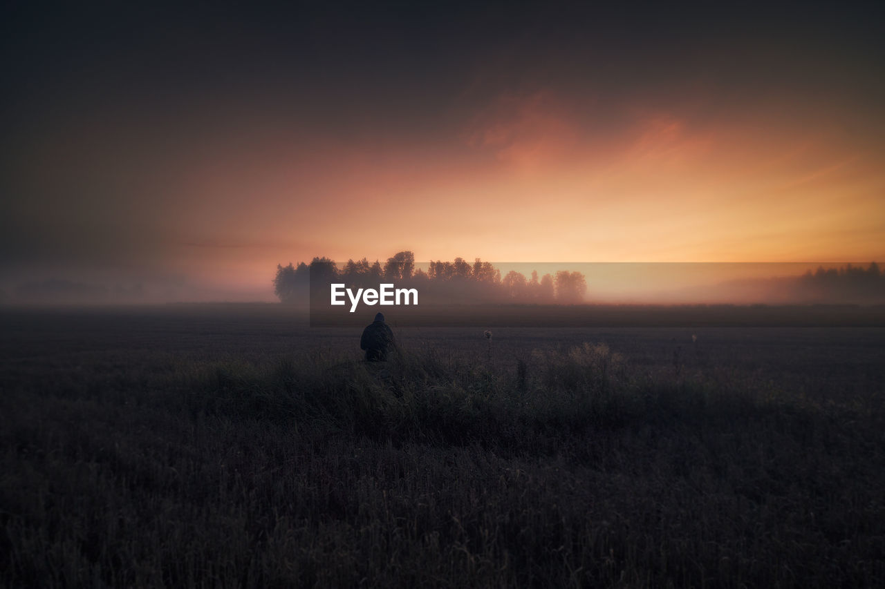 Man standing on field against sky during sunset