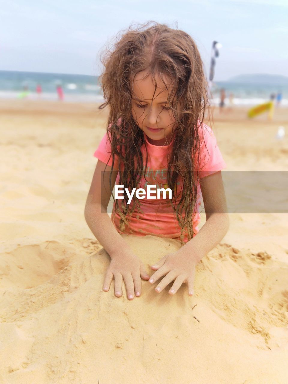 Girl playing with sand at beach against sky