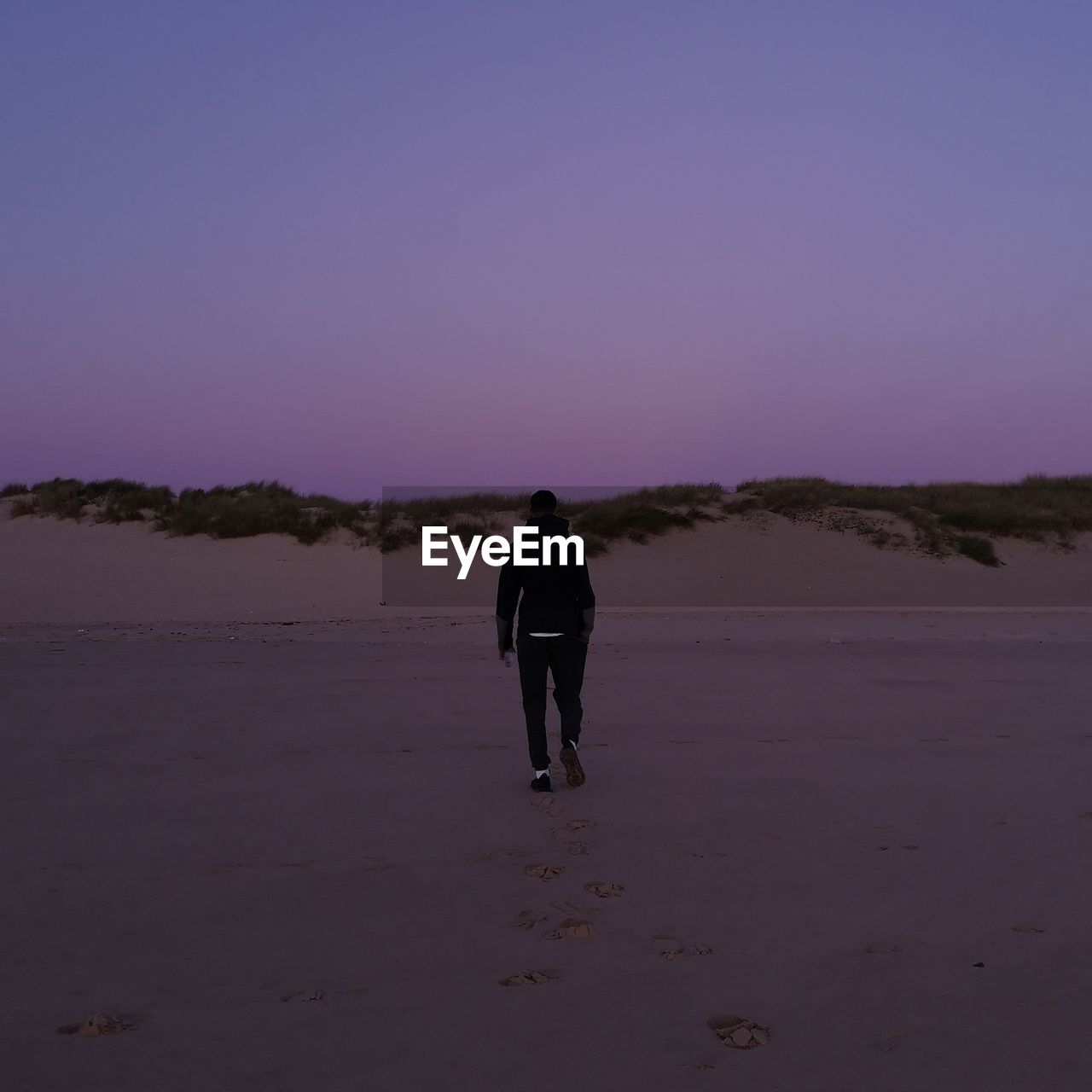 Rear view of man walking at desert during sunset