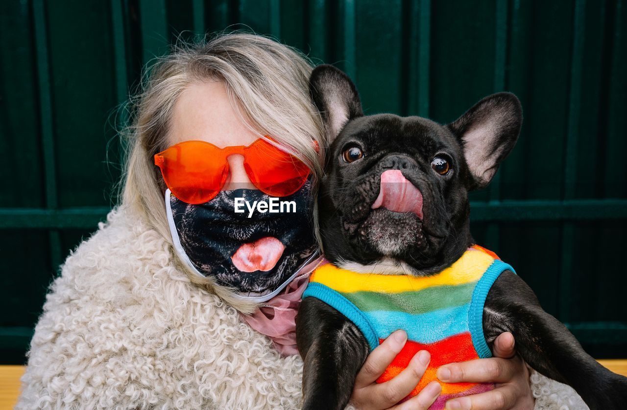 Portrait of woman with mask holding small french bulldog dog