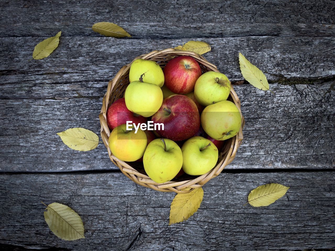 Red and yellow apples in a wooden basket placed on a rustic wooden table