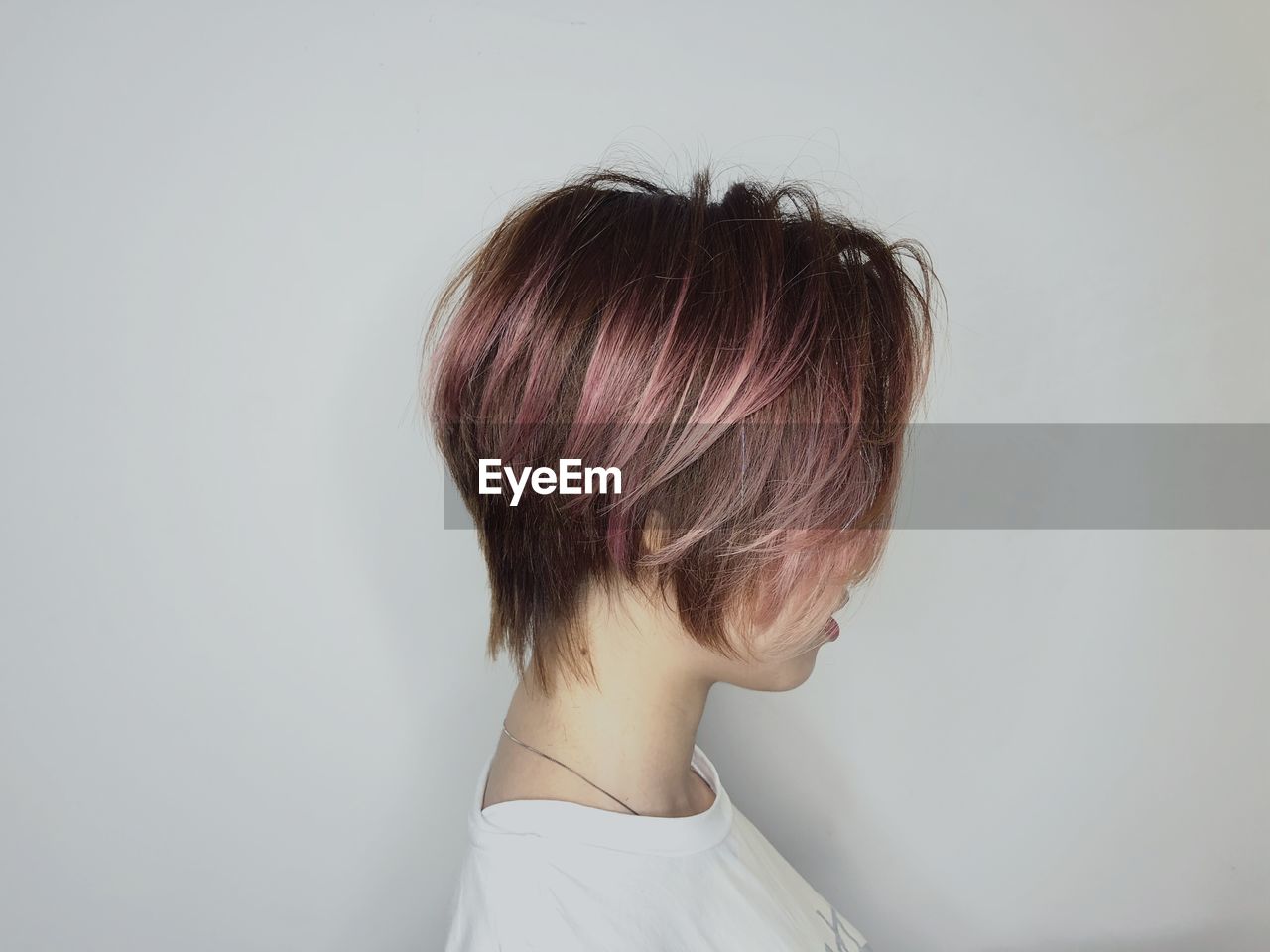 Side view of young woman with dyed hair against white background