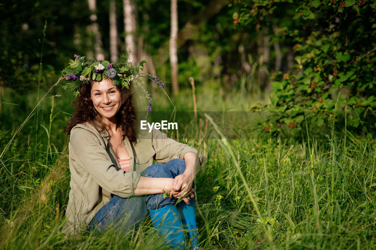 Cheerful rural woman enjoying nature in rubber boots and wildflower wreath