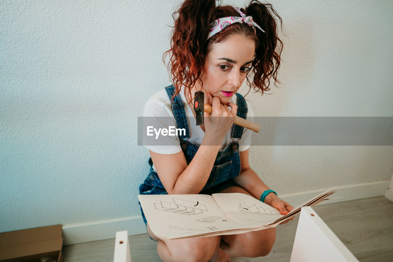 YOUNG WOMAN LOOKING AWAY WHILE STANDING AGAINST WALL