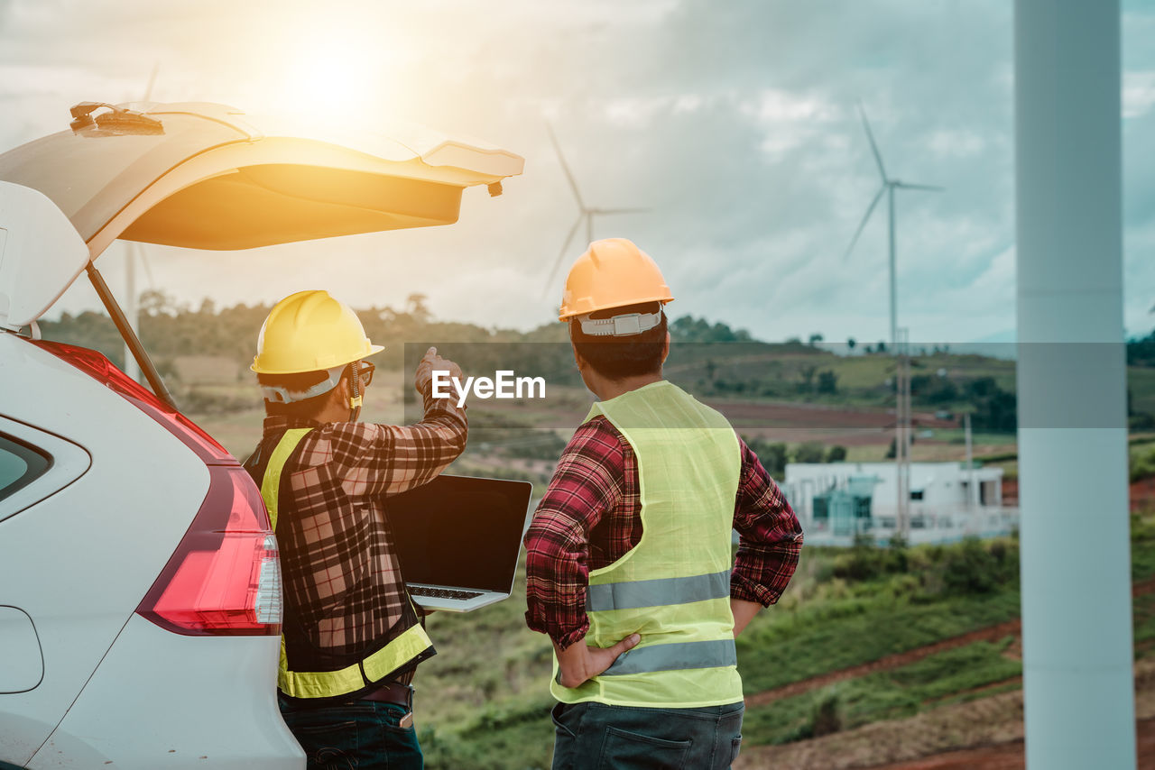 Rear view of man pointing towards windmill by colleague on land