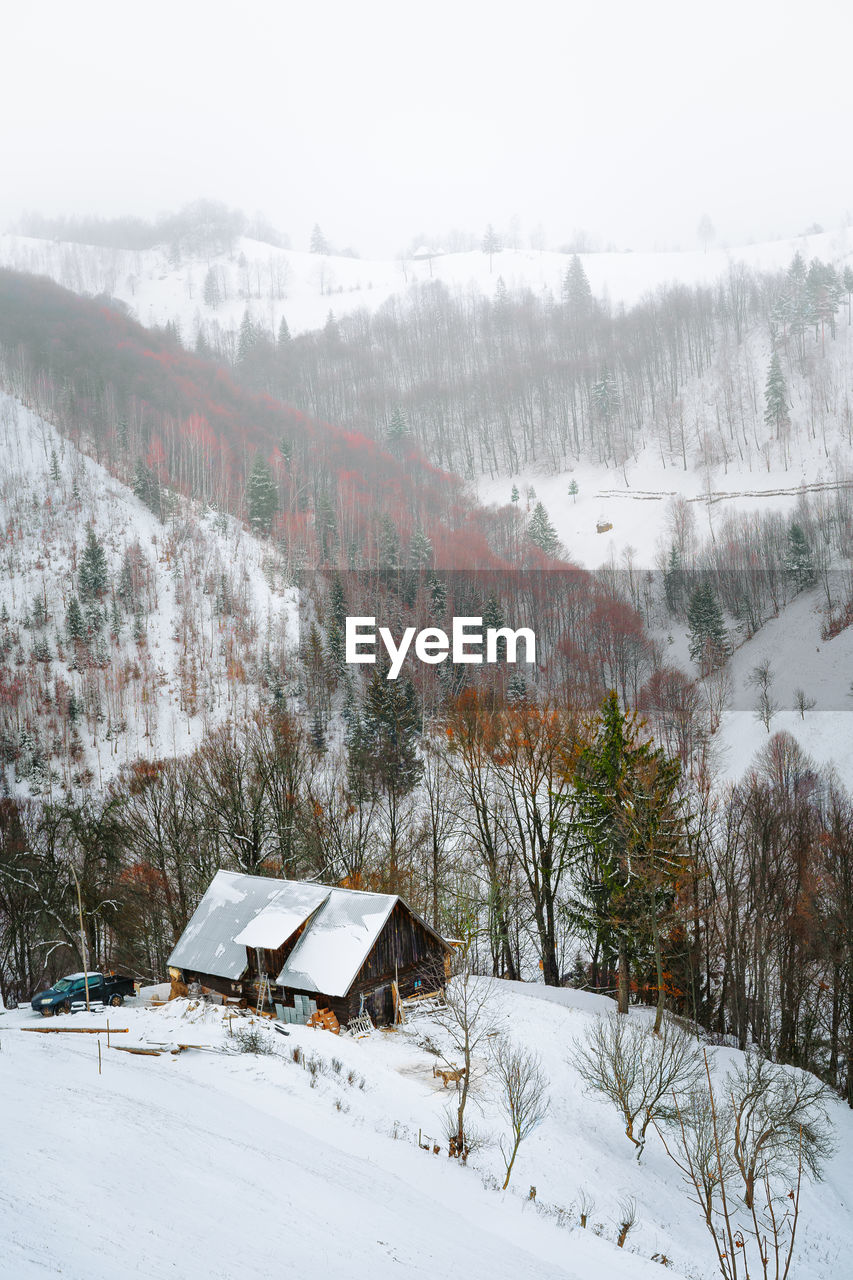 Scenic view of cabin and snowcapped mountains in a winter foggy day