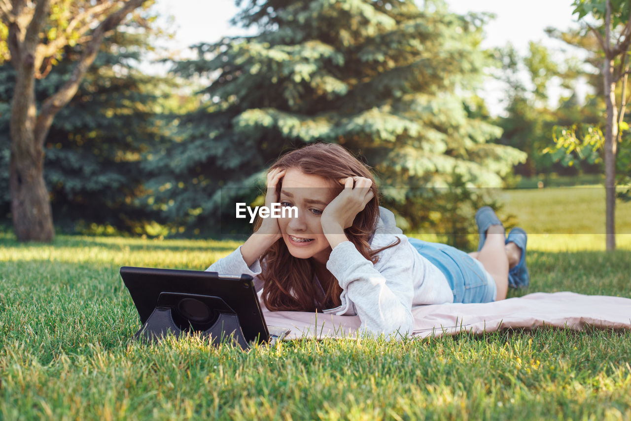 Worried young woman using tablet while lying on grass