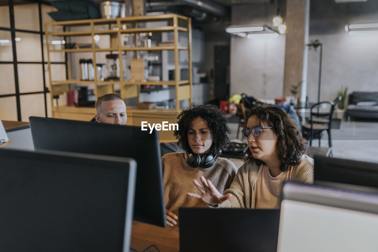 Young female hacker explaining strategy to colleagues over computer while working in office