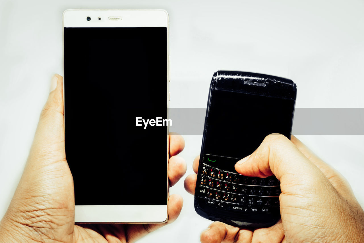 Cropped hands holding mobile phones against white background