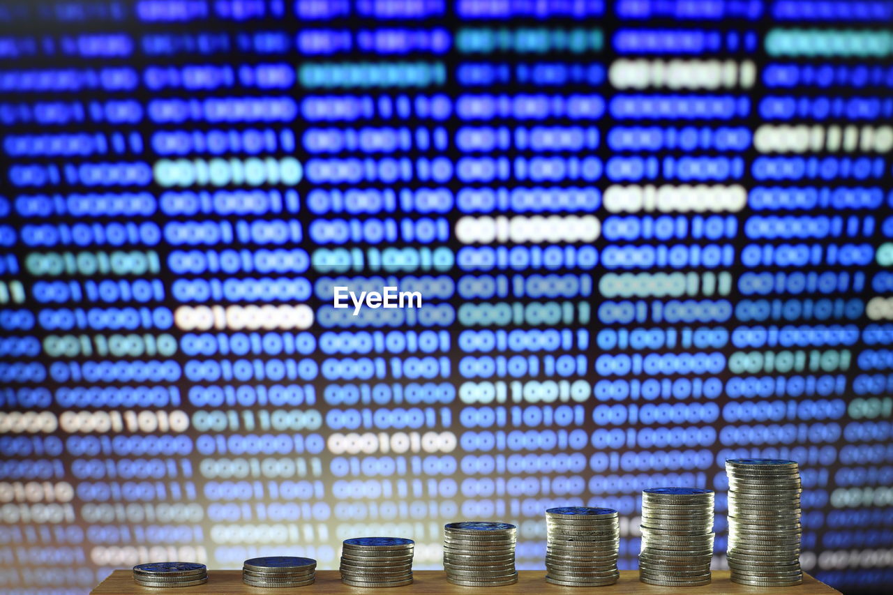 Stacked coins against binary code on screen