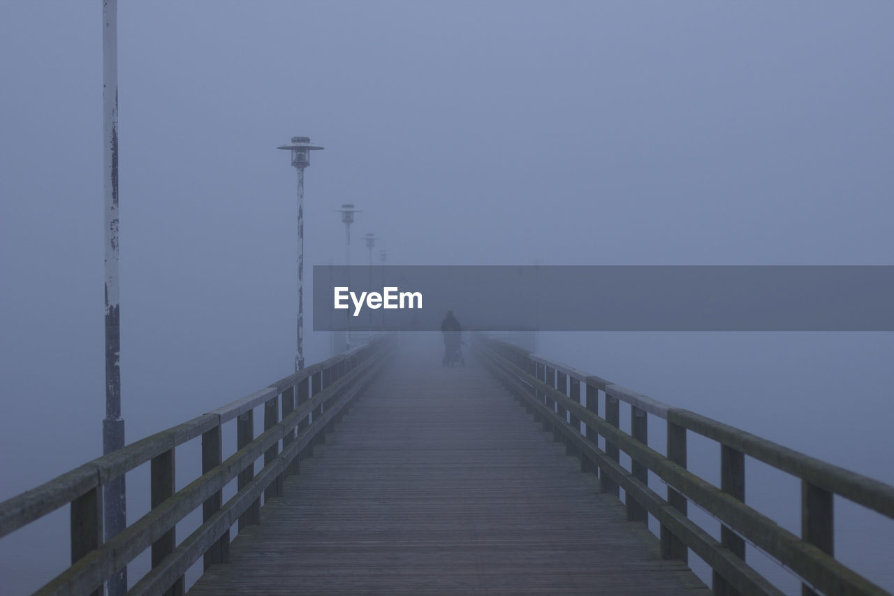 MAN WALKING ON FOOTBRIDGE AGAINST SKY