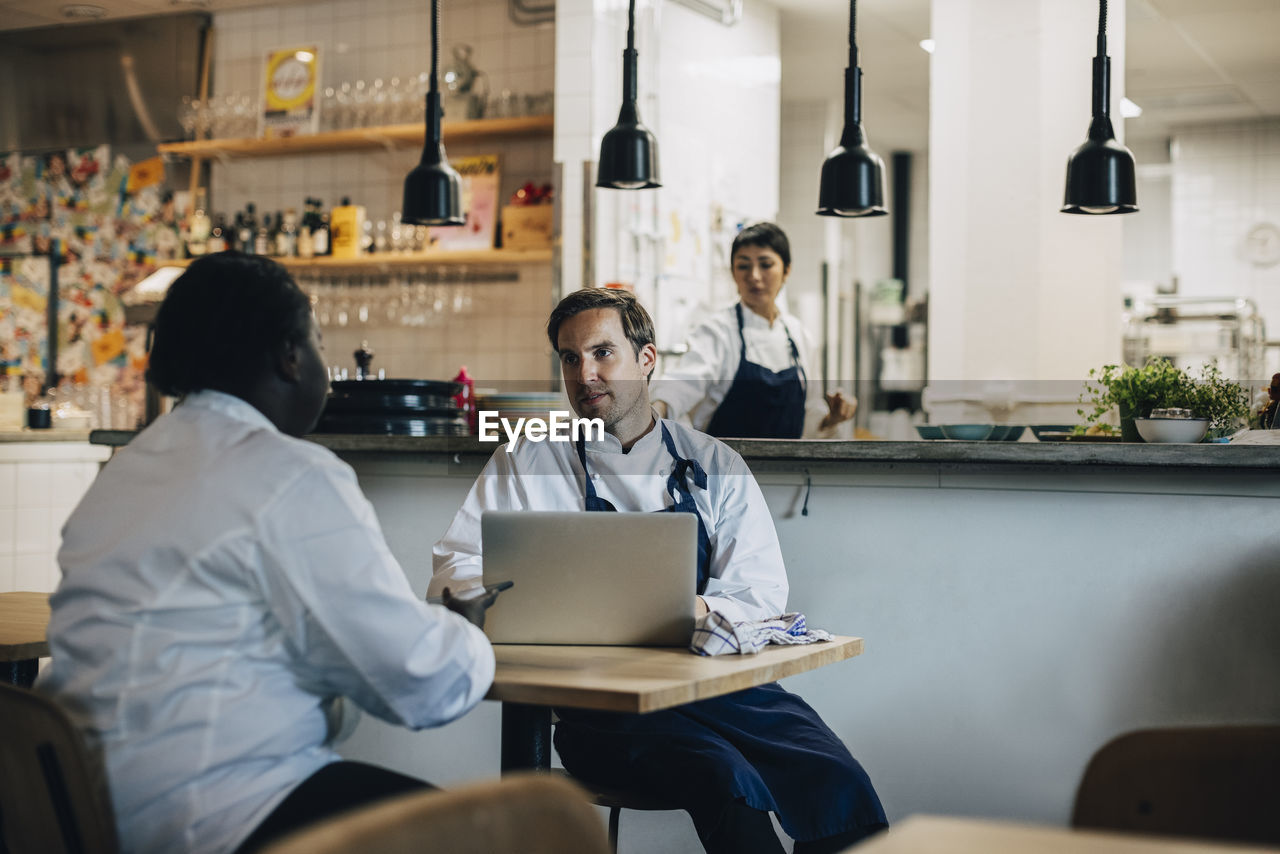 Multiracial chefs discussing business strategy while sitting at table in restaurant